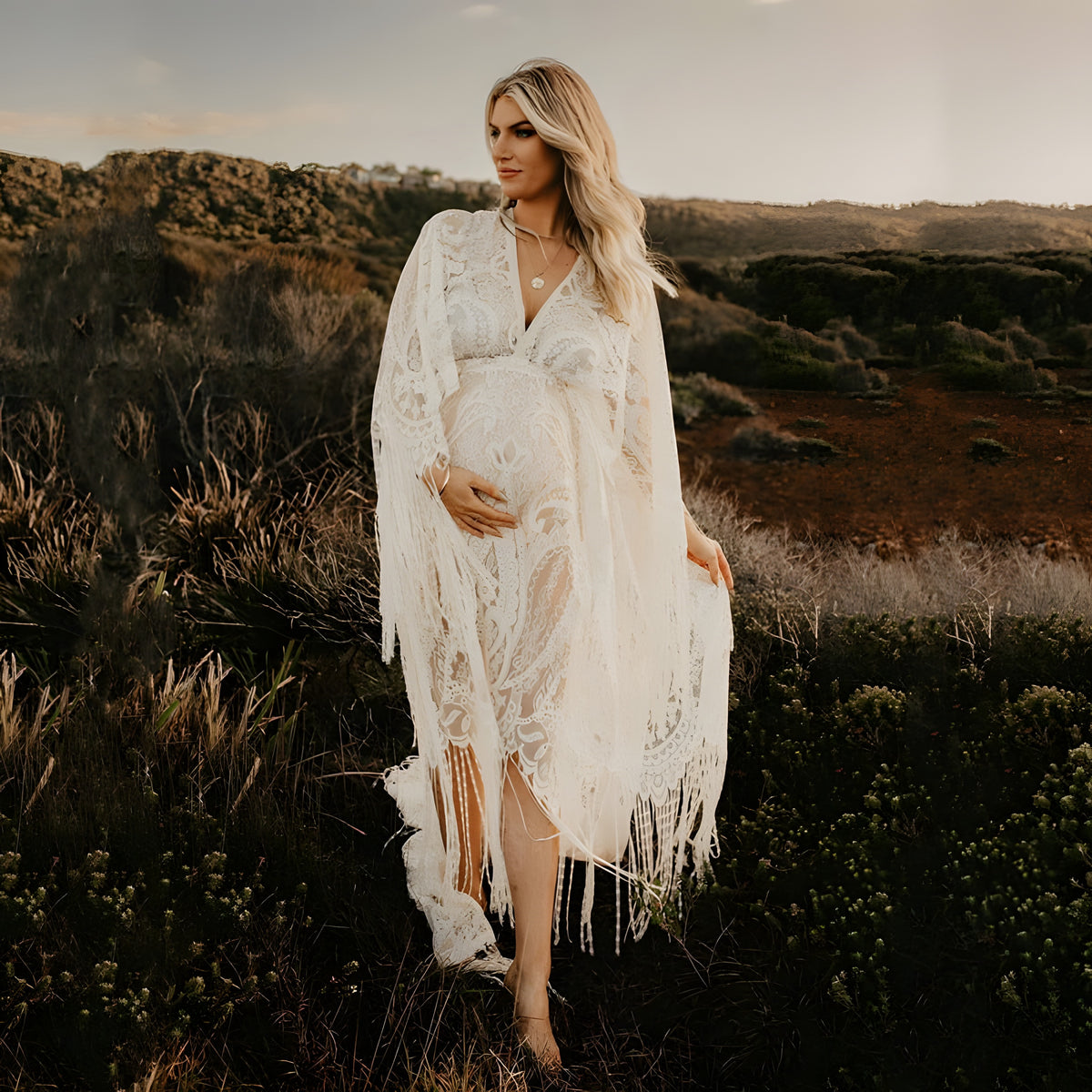 Robe de grossesse bohème en dentelle ivoire portée par un modèle souriant au coucher de soleil