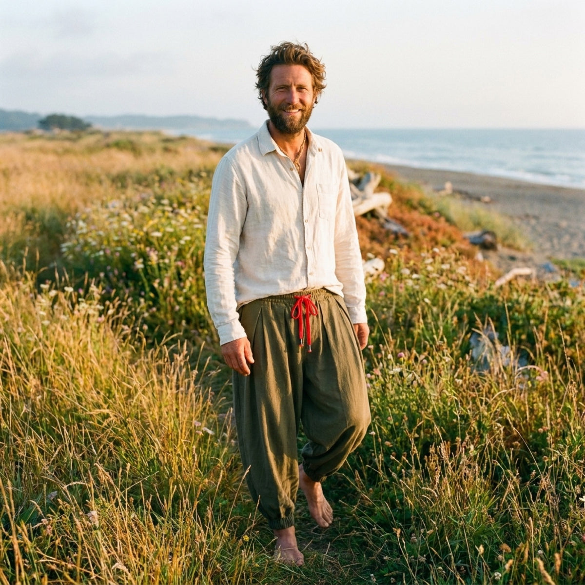Homme souriant portant le sarouel homme en lin vert kaki, cordon rouge, dans un champ au coucher du soleil