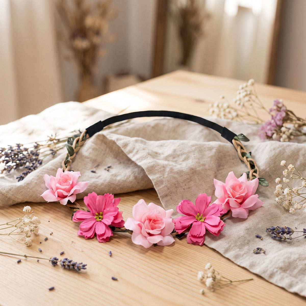 Couronne de fleurs rose en tissu posée sur une table en bois avec du lin et des fleurs séchées