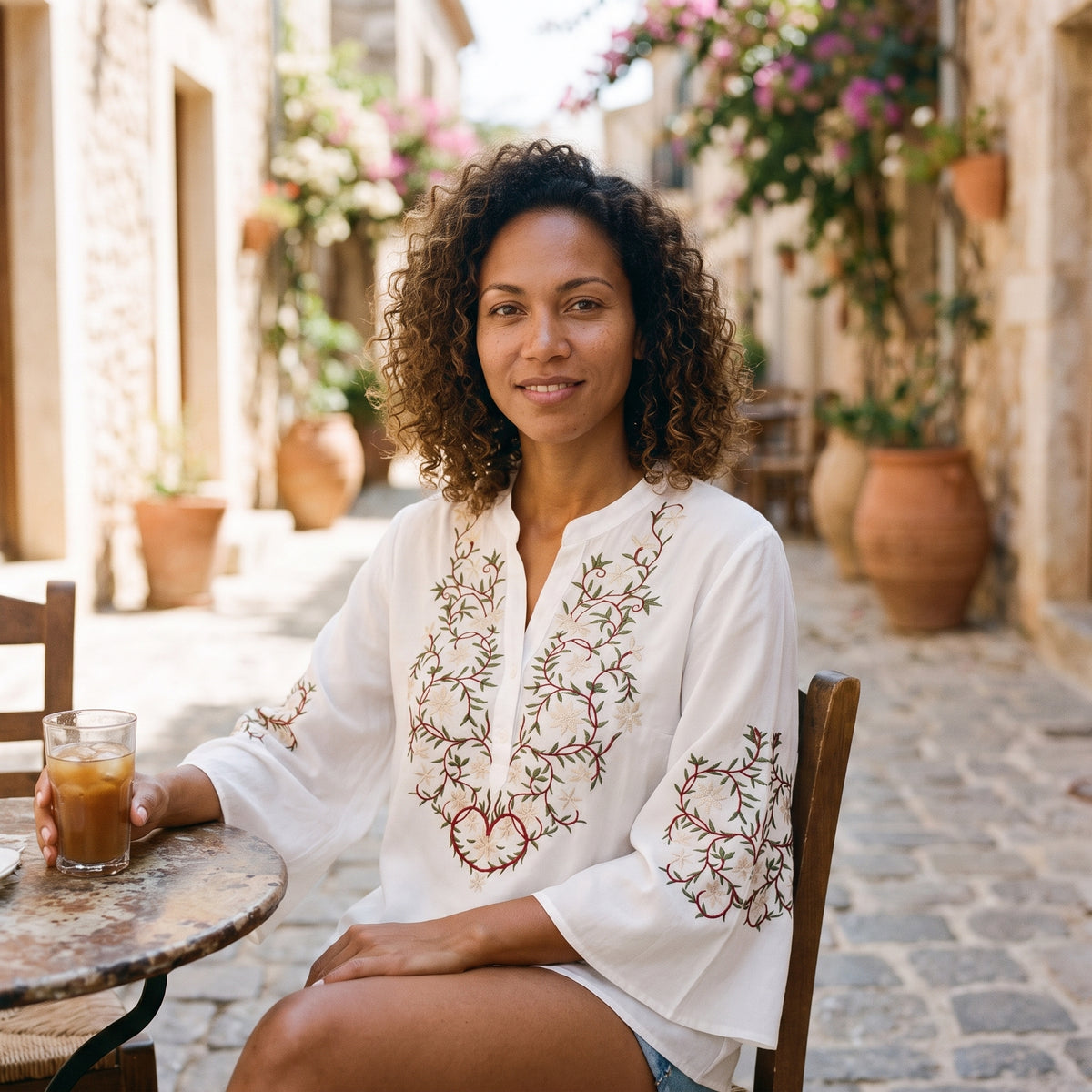 Modèle souriante portant la chemise blanche brodée, assise à une terrasse méditerranéenne Image