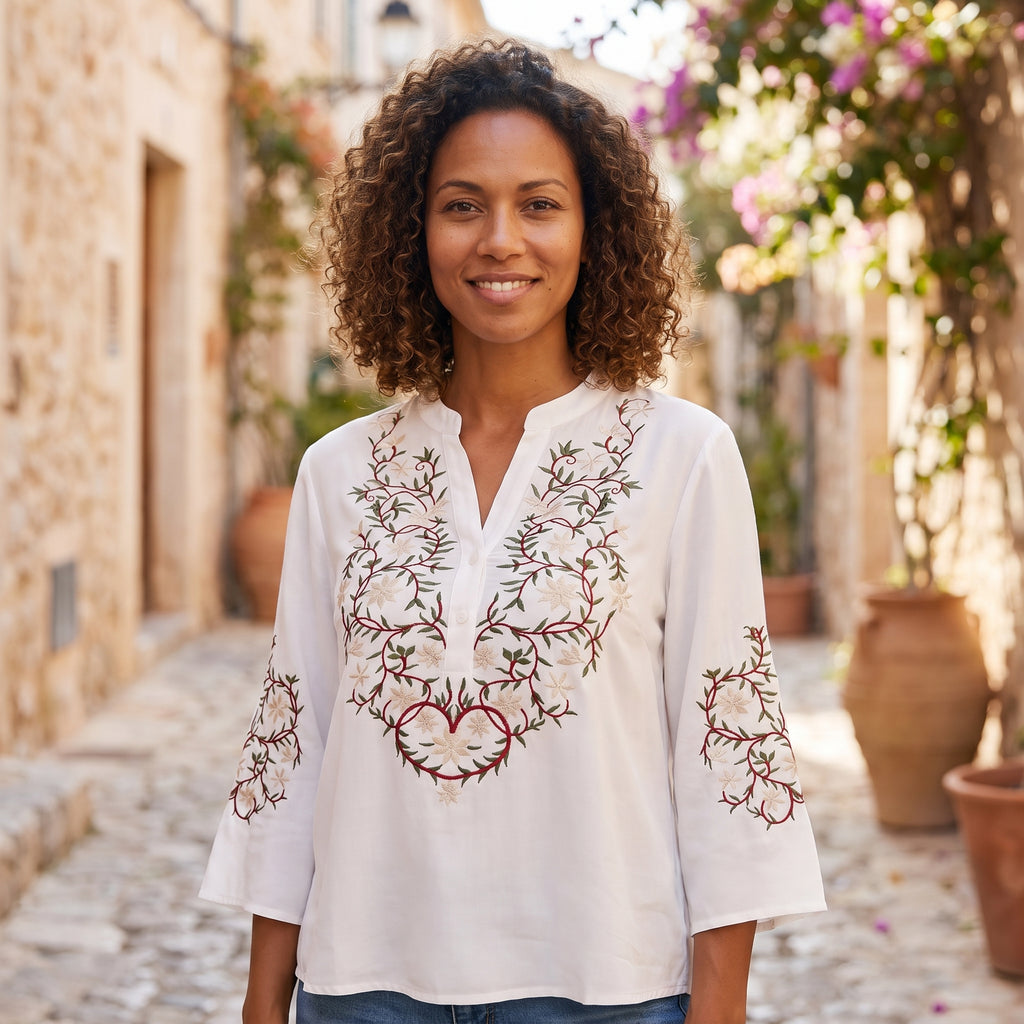 Modèle souriante portant la chemise blanche brodée, ruelle méditerranéenne pavée