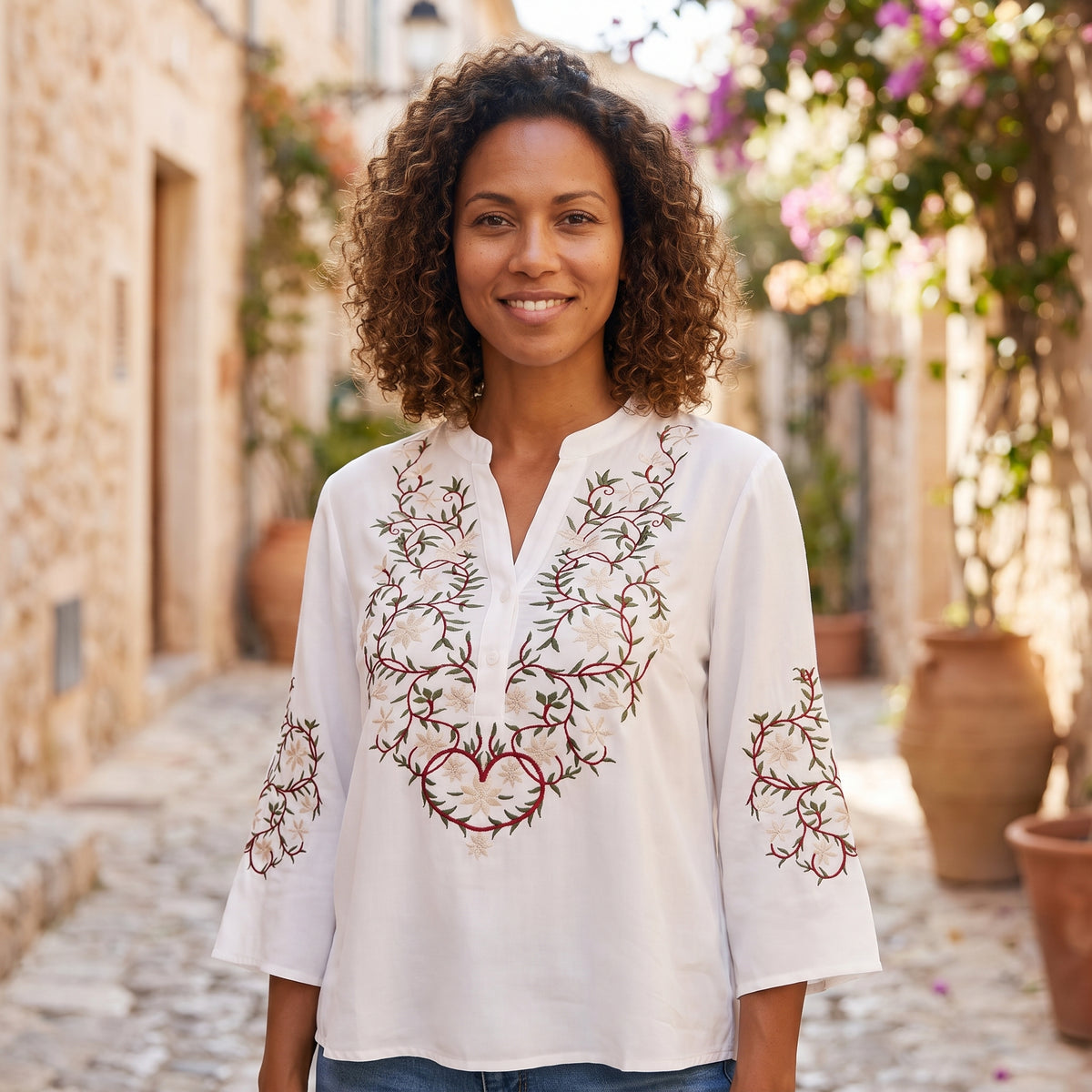 Modèle souriante portant la chemise blanche brodée, ruelle méditerranéenne pavée