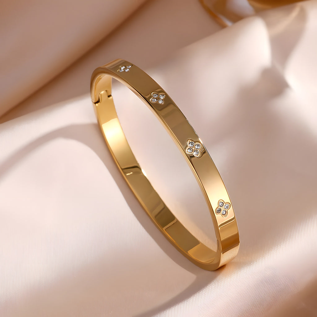 Bracelet jonc or à motifs quadrilobes sertis de zircons, fermoir clip, sur satin champagne