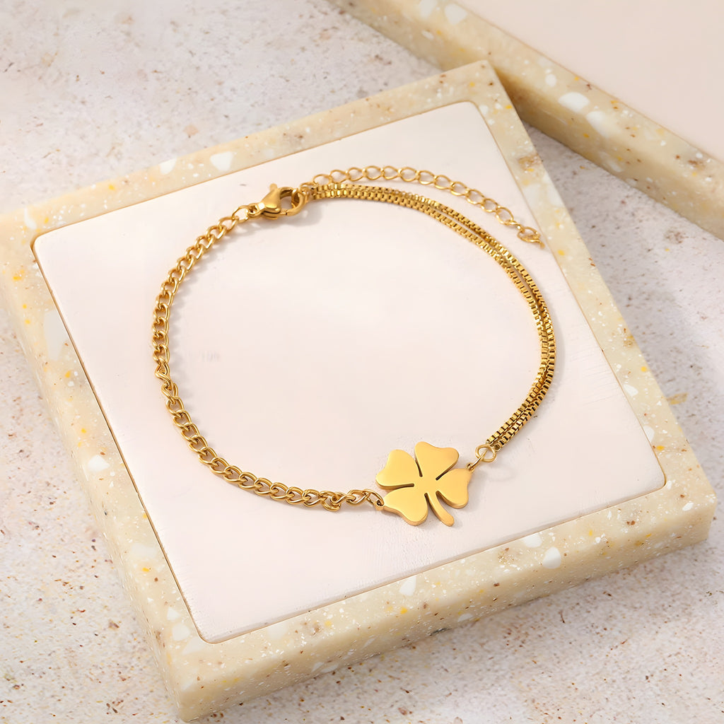 Bracelet trèfle 4 feuilles doré à plat sur plateau beige, double chaîne asymétrique