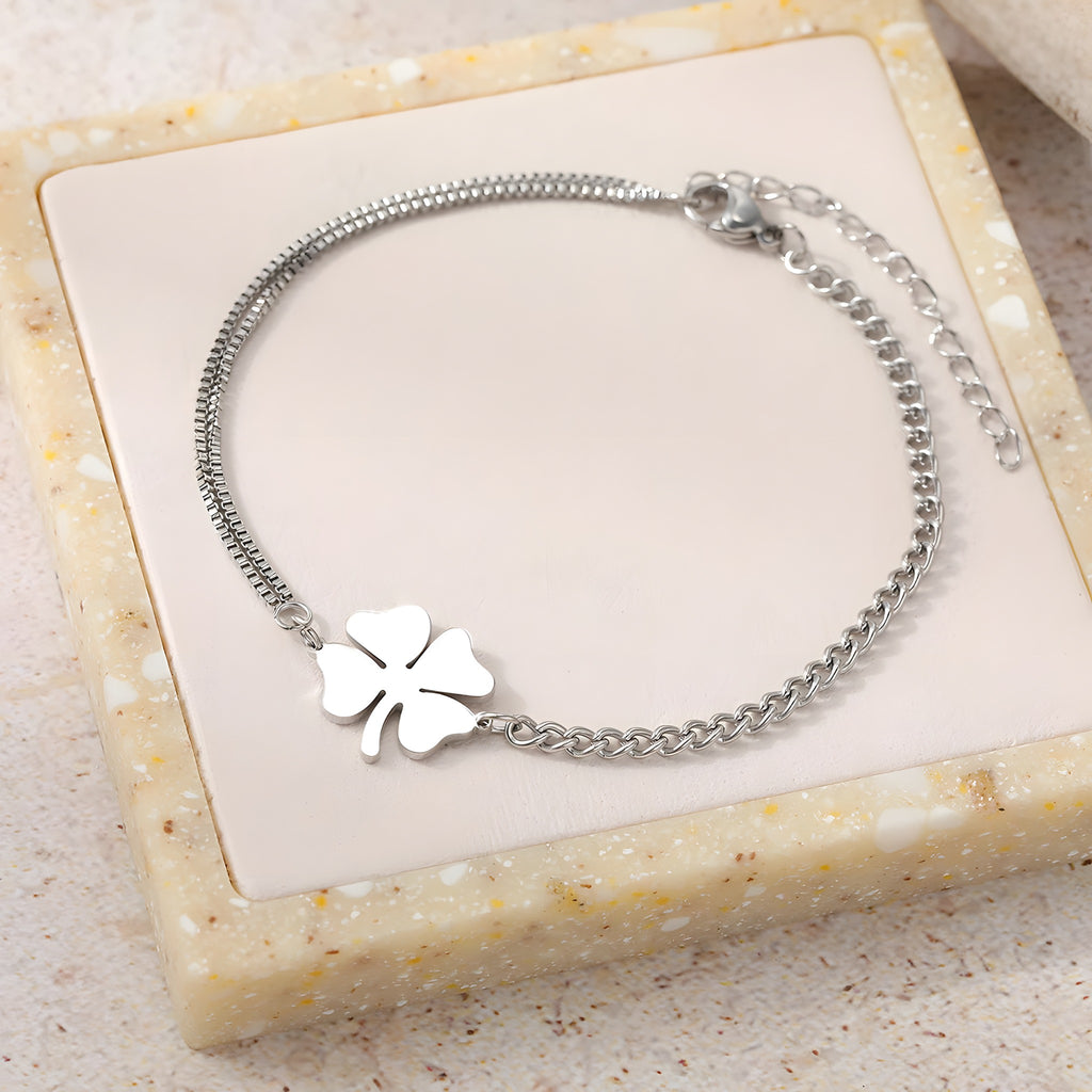 Bracelet trèfle 4 feuilles argenté à plat sur plateau beige, double chaîne asymétrique
