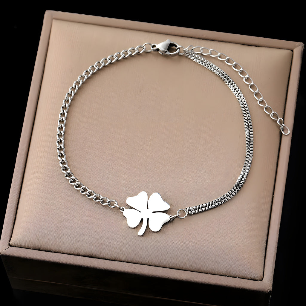 Bracelet trèfle 4 feuilles argenté à plat dans un écrin beige, chaîne asymétrique