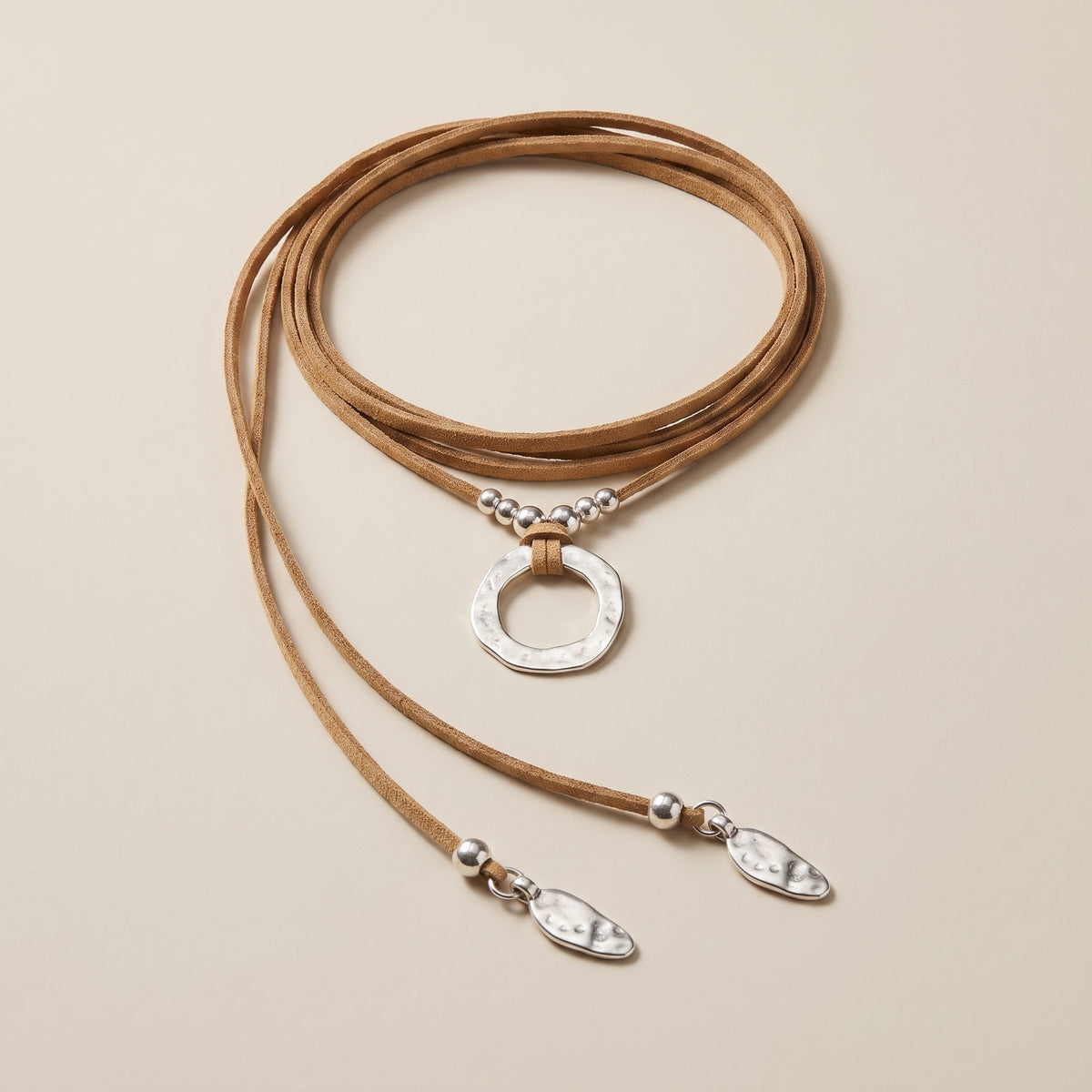 Collier en suédine camel et anneau martelé argenté, posé à plat sur fond écru