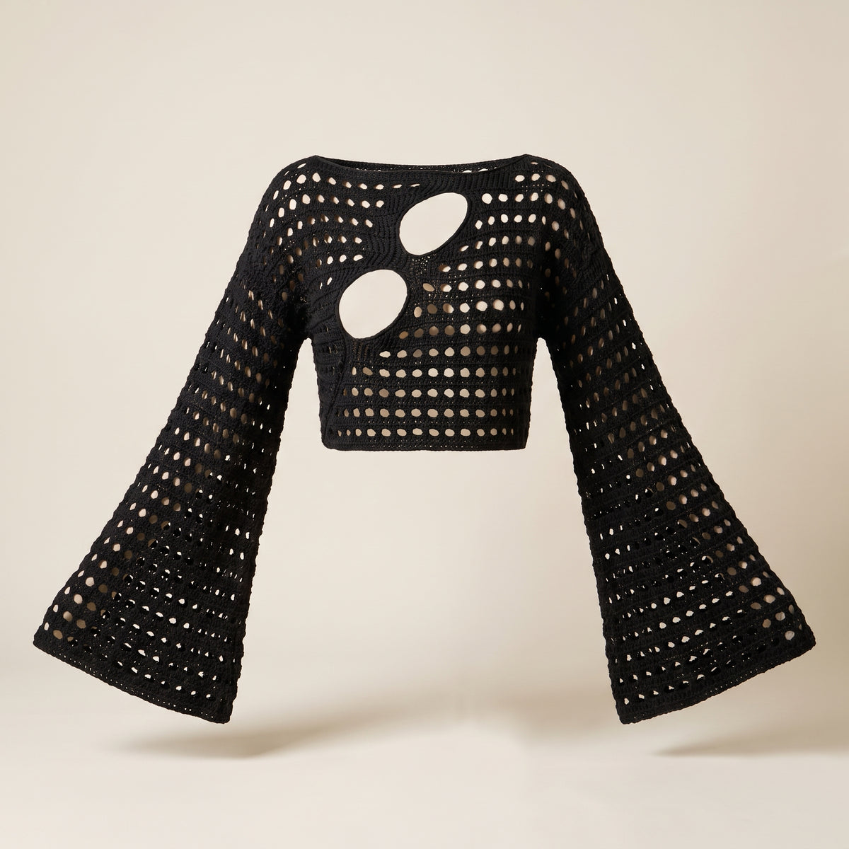 Crop top au crochet noir vu de face sur fond écru, manches longues évasées
