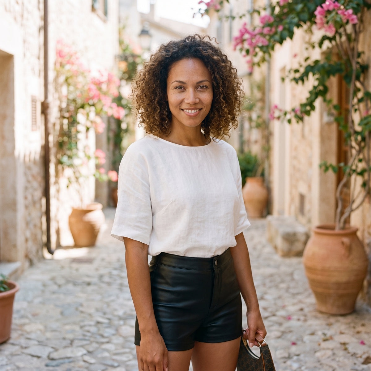 Modèle souriante portant le mini short en simili cuir noir taille haute, ruelle méditerranéenne pavée