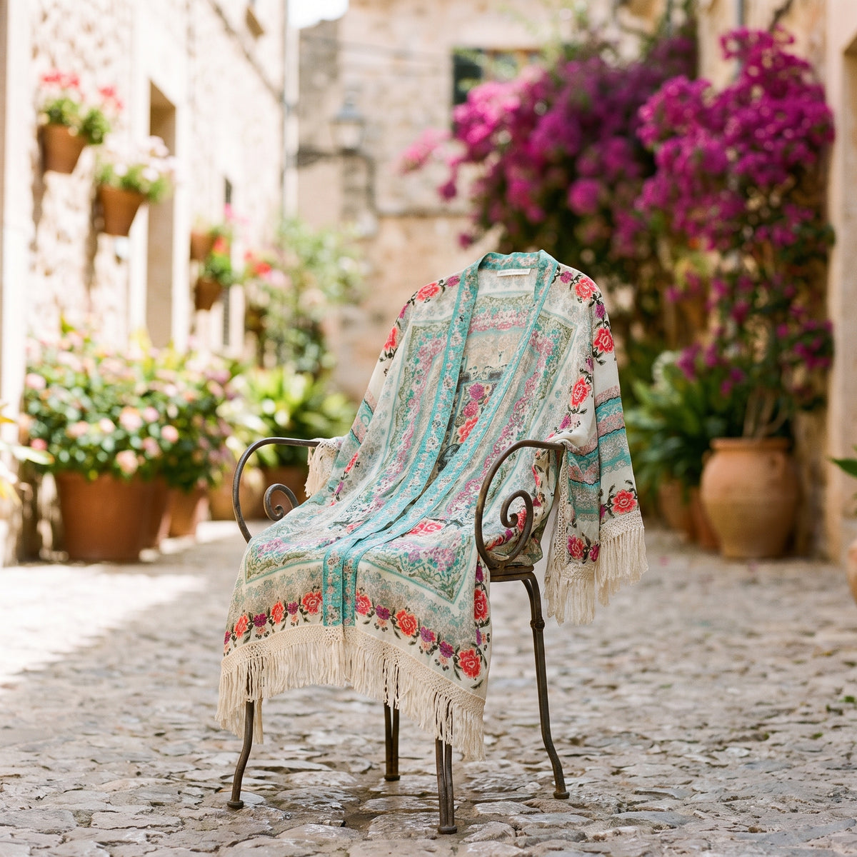 Gilet kimono fleuri à franges posé sur une chaise dans une ruelle méditerranéenne