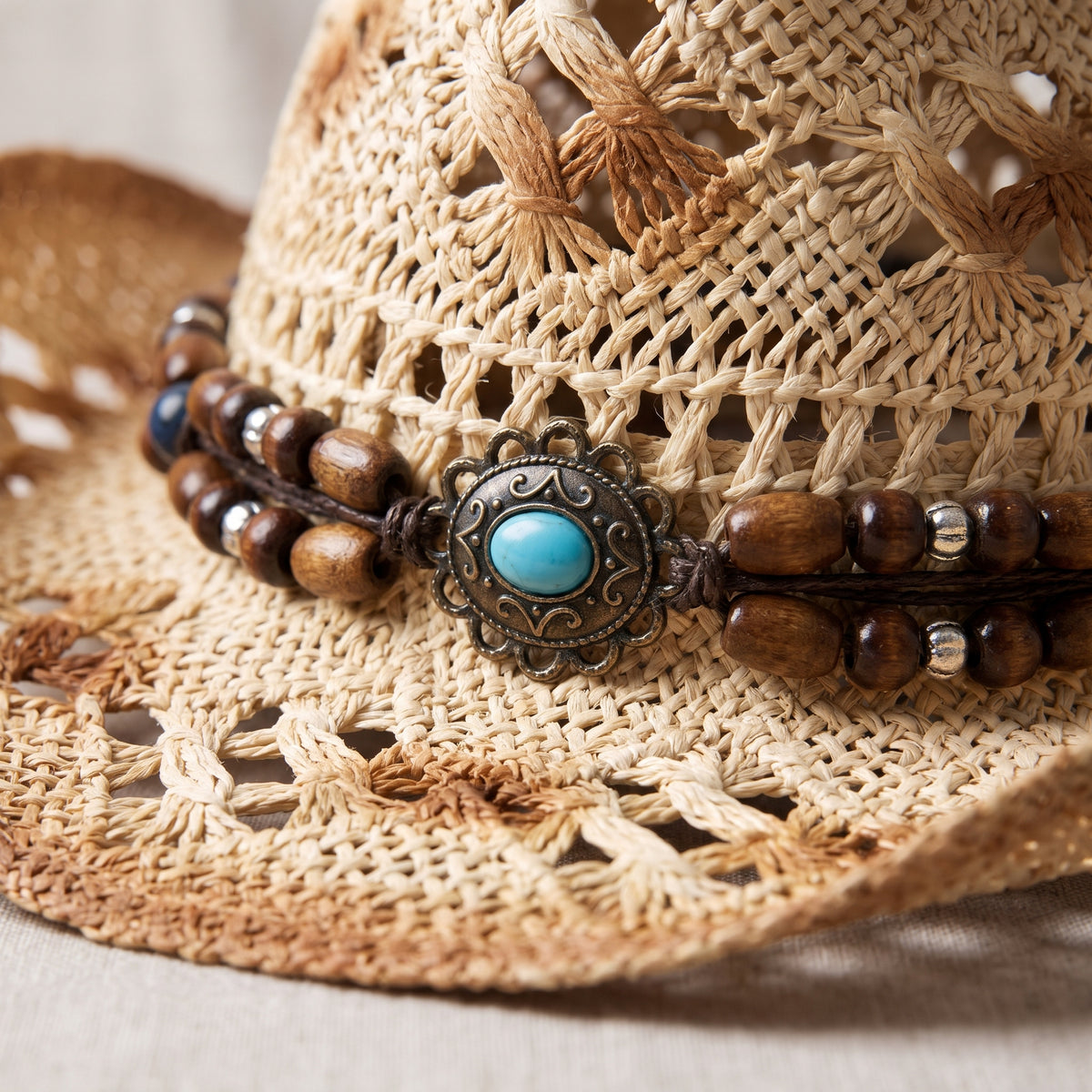Gros plan sur le bandeau de perles en bois et le médaillon turquoise du chapeau de paille hippie chic