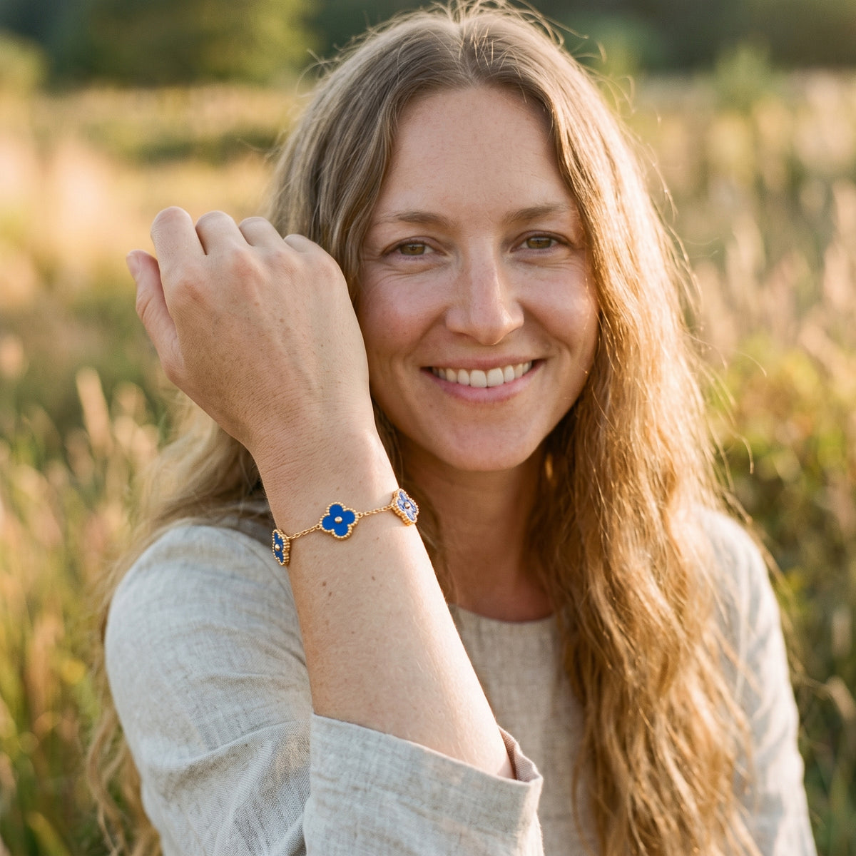 Femme souriante portant le bracelet trèfle doré à fleurs bleu