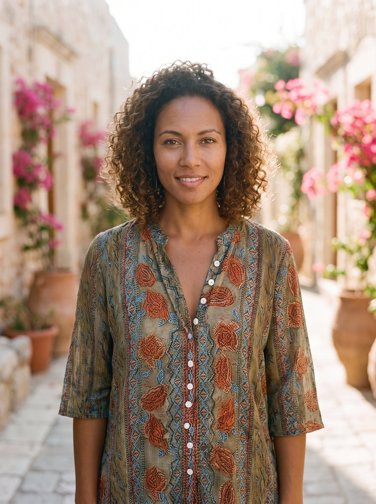 Modèle souriante portant la chemise hippie à fleurs coloris beige, encolure en V, ruelle méditerranéenne