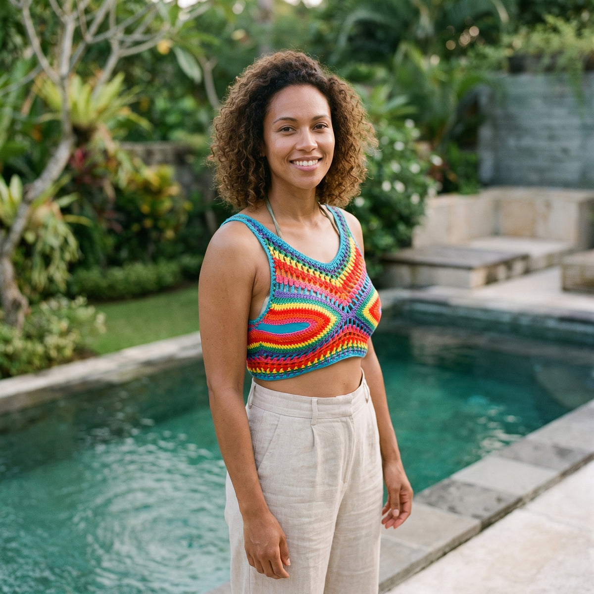 Crop-top au crochet arc-en-ciel dominante bleue porté par un modèle souriant au bord d'une piscine
