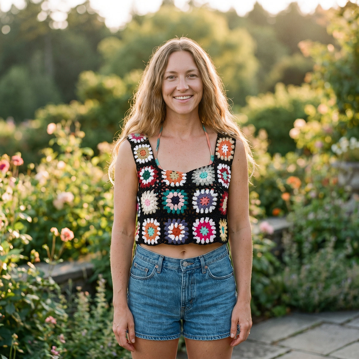 Crop-top au crochet granny squares fond noir porté par un modèle souriant dans un jardin