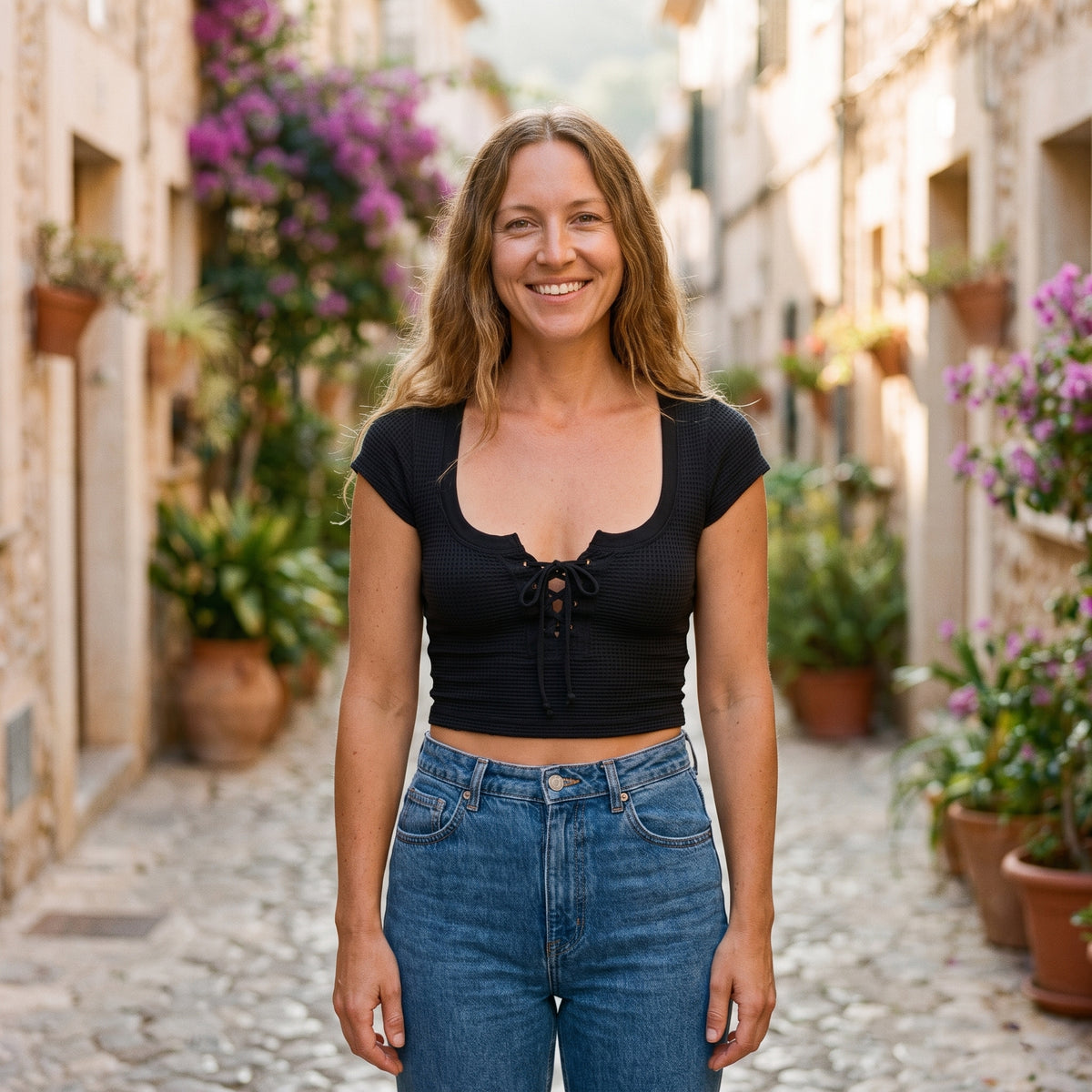 Crop-top maille gaufrée noir à laçage porté par un modèle souriant en ruelle méditerranéenne