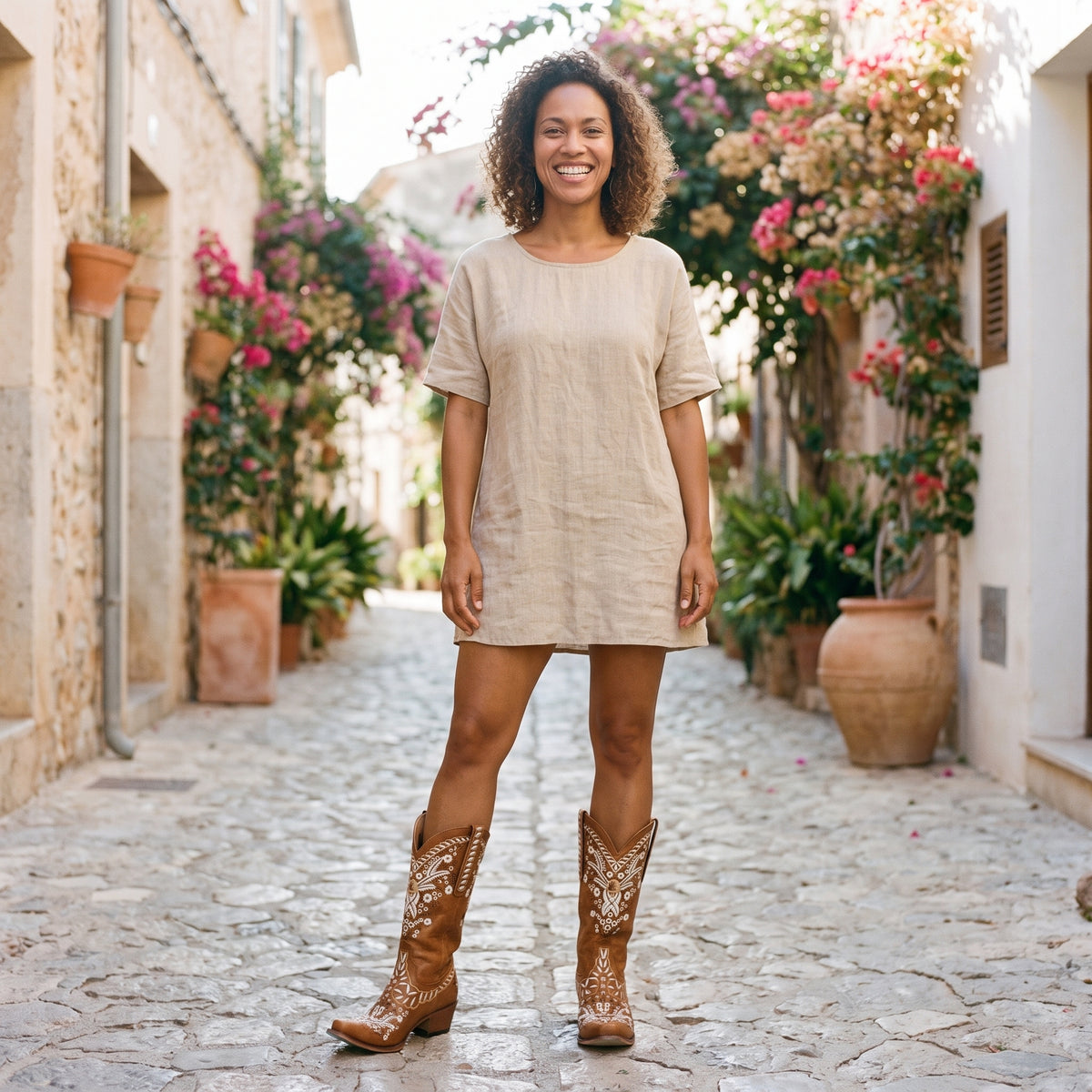 Modèle souriante portant les bottes western camel à fleurs brodées dans une ruelle méditerranéenne