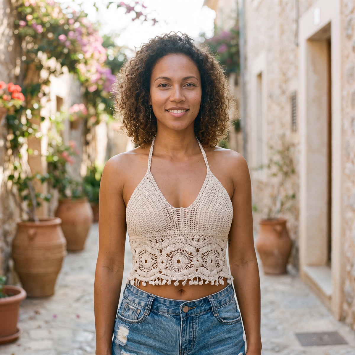 Crop top au crochet écru porté par un modèle souriant dans une ruelle ensoleillée