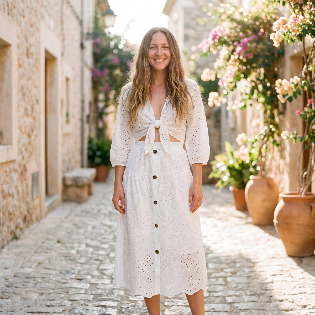 Jupe midi blanche en broderie anglaise portée par un modèle souriant en ruelle méditerranéenne