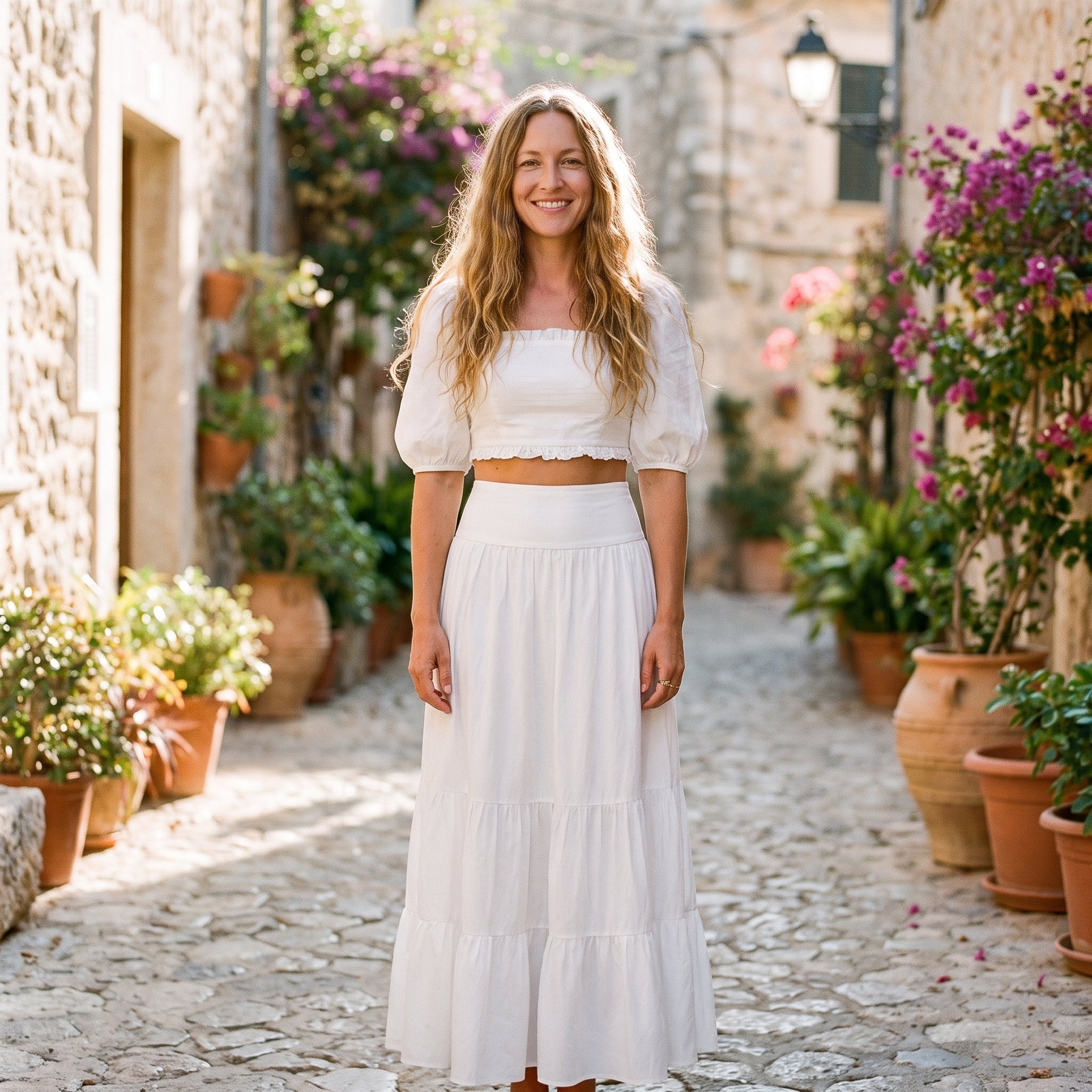 Jupe longue blanche à volants portée par un modèle souriant en ruelle méditerranéenne Image