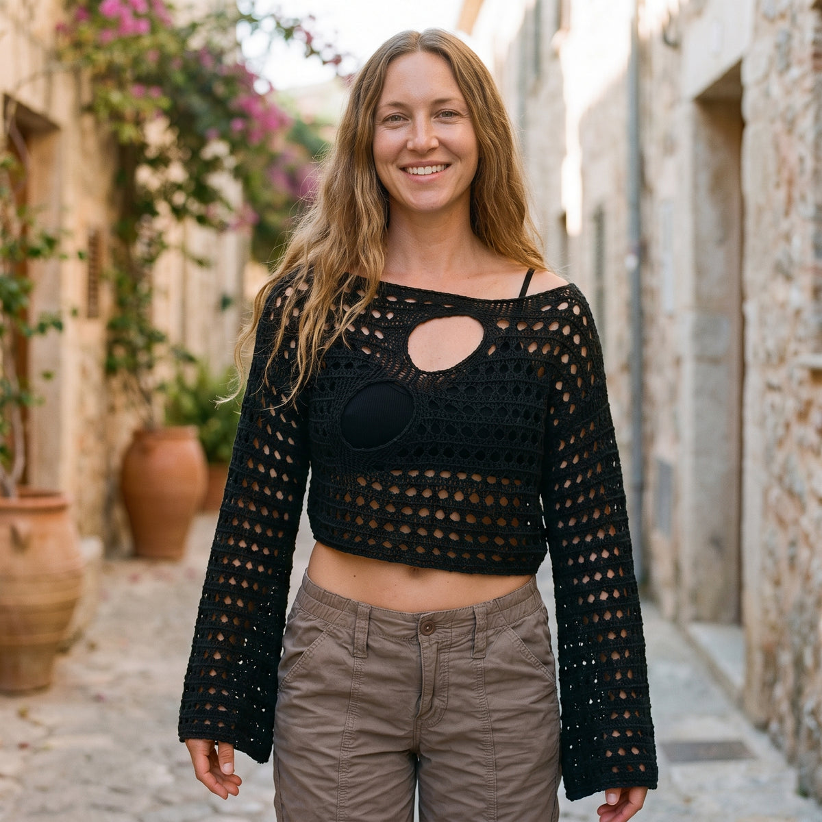Crop top au crochet noir ajouré porté par un modèle souriant dans une ruelle