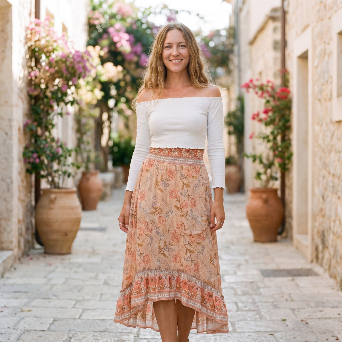 Jupe midi bohème pêche à fleurs portée par un modèle souriant en ruelle méditerranéenne
