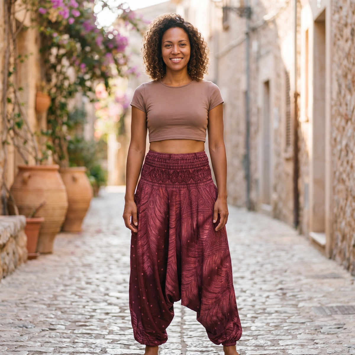 Modèle souriante portant le sarouel femme bordeaux à imprimé plume de paon, ruelle méditerranéenne