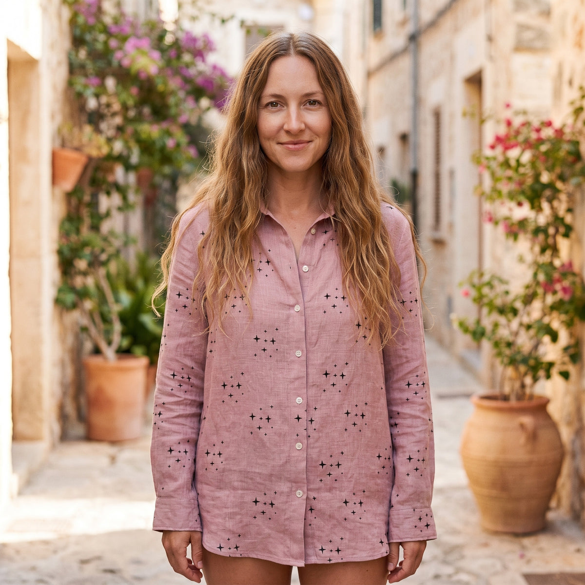 Modèle souriante portant la chemise hippie chic rose à petites étoiles, manches longues, ruelle méditerranéenne pavée