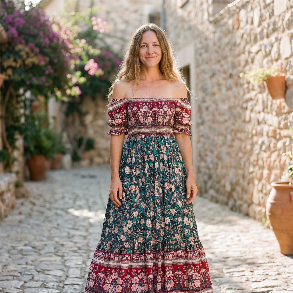 Modèle souriante portant la robe longue bohème fleurie verte à épaules dénudées, ruelle méditerranéenne